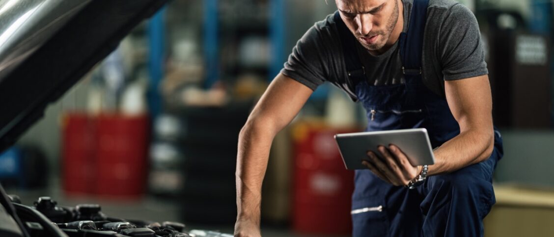 Une homme en train de bricoler sur sa voiture en même temps qu'il cherche les bonnes pièces sur internet