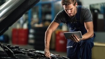 Une homme en train de bricoler sur sa voiture en même temps qu'il cherche les bonnes pièces sur internet