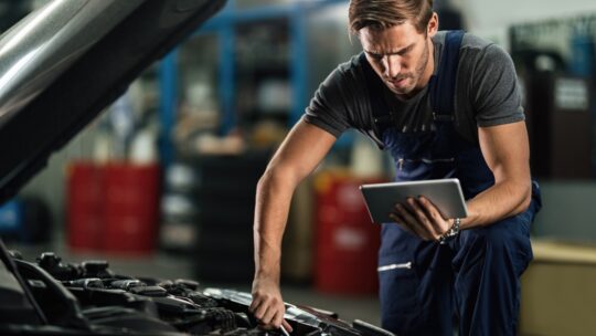 Une homme en train de bricoler sur sa voiture en même temps qu'il cherche les bonnes pièces sur internet