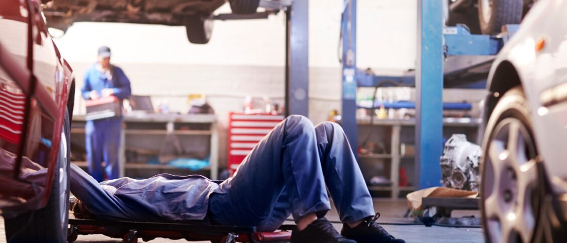Un mécanicien effectuant une réparation sous un véhicule dans un garage, illustrant l'entretien automobile avec des pièces d'occasion