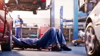 Un mécanicien effectuant une réparation sous un véhicule dans un garage, illustrant l'entretien automobile avec des pièces d'occasion