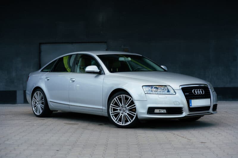 Audi A6 grise, une grande berline d'occasion vue de trois quarts avant garée devant un mur sombre